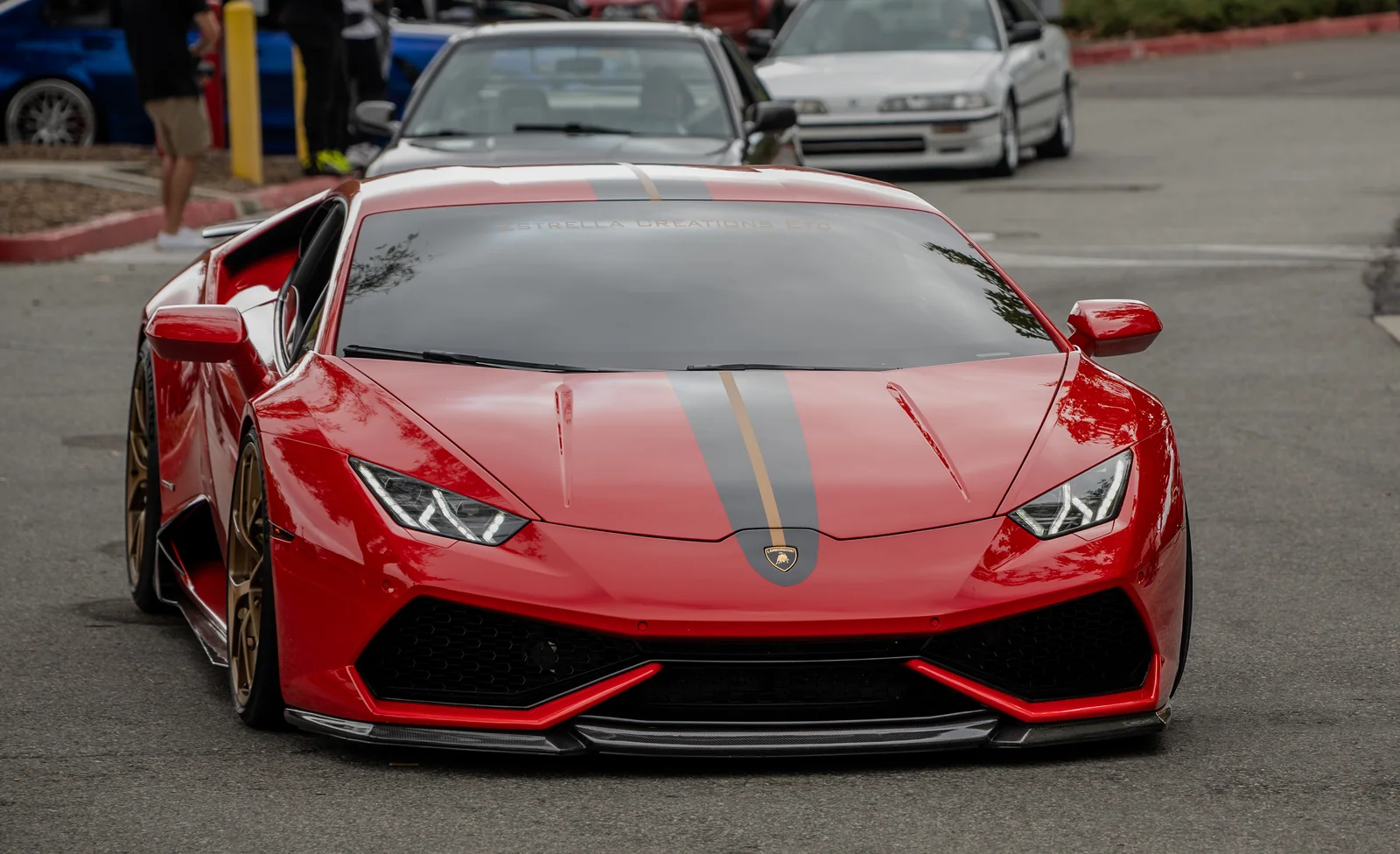 Red Lamborghini viewed nearly head-on, with a gray hood stripe, gold accent, and low front splitter.