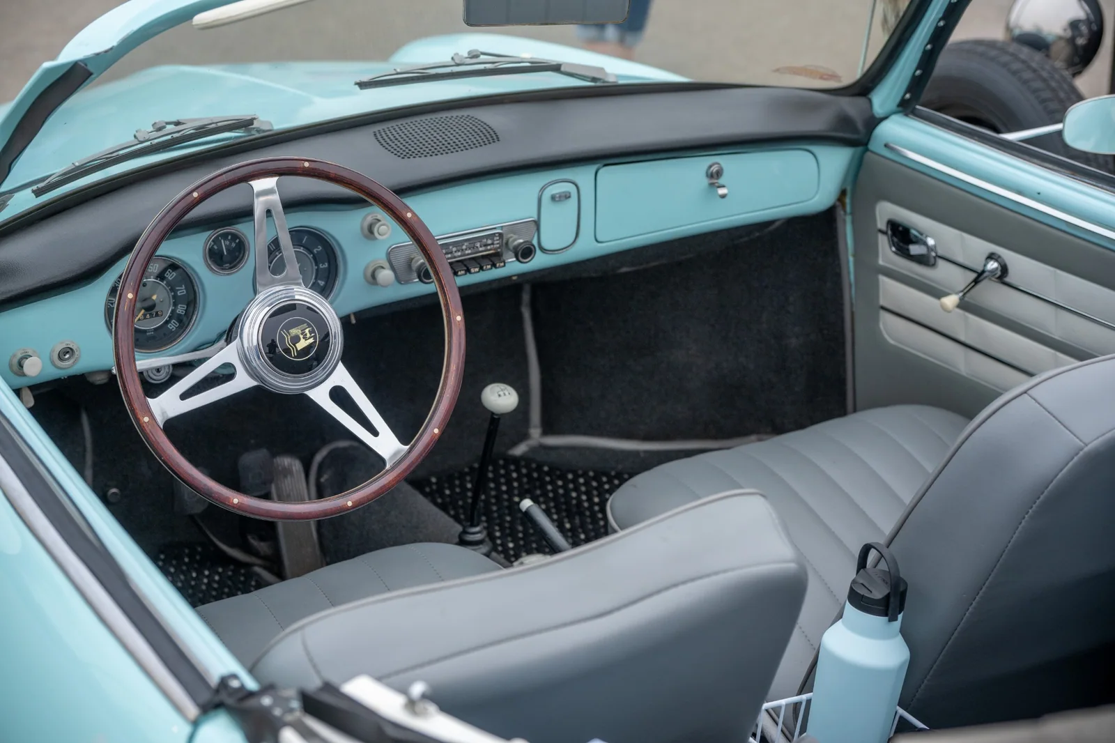 Karmann Ghia interior with a seafoam dashboard, wood-rimmed steering wheel, round instruments, radio, ivory-colored gear knob, and gray seats.