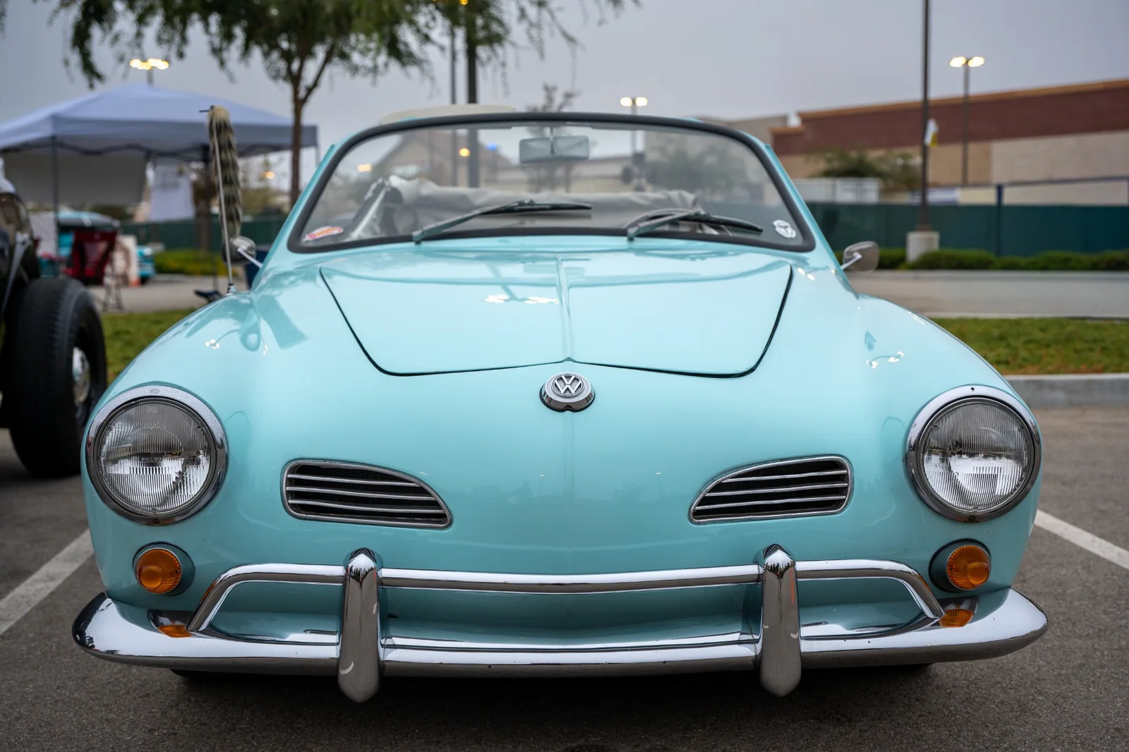 Seafoam Volkswagen Karmann Ghia convertible viewed head-on, with round headlights, a VW nose badge, amber indicators, and a chrome bumper.