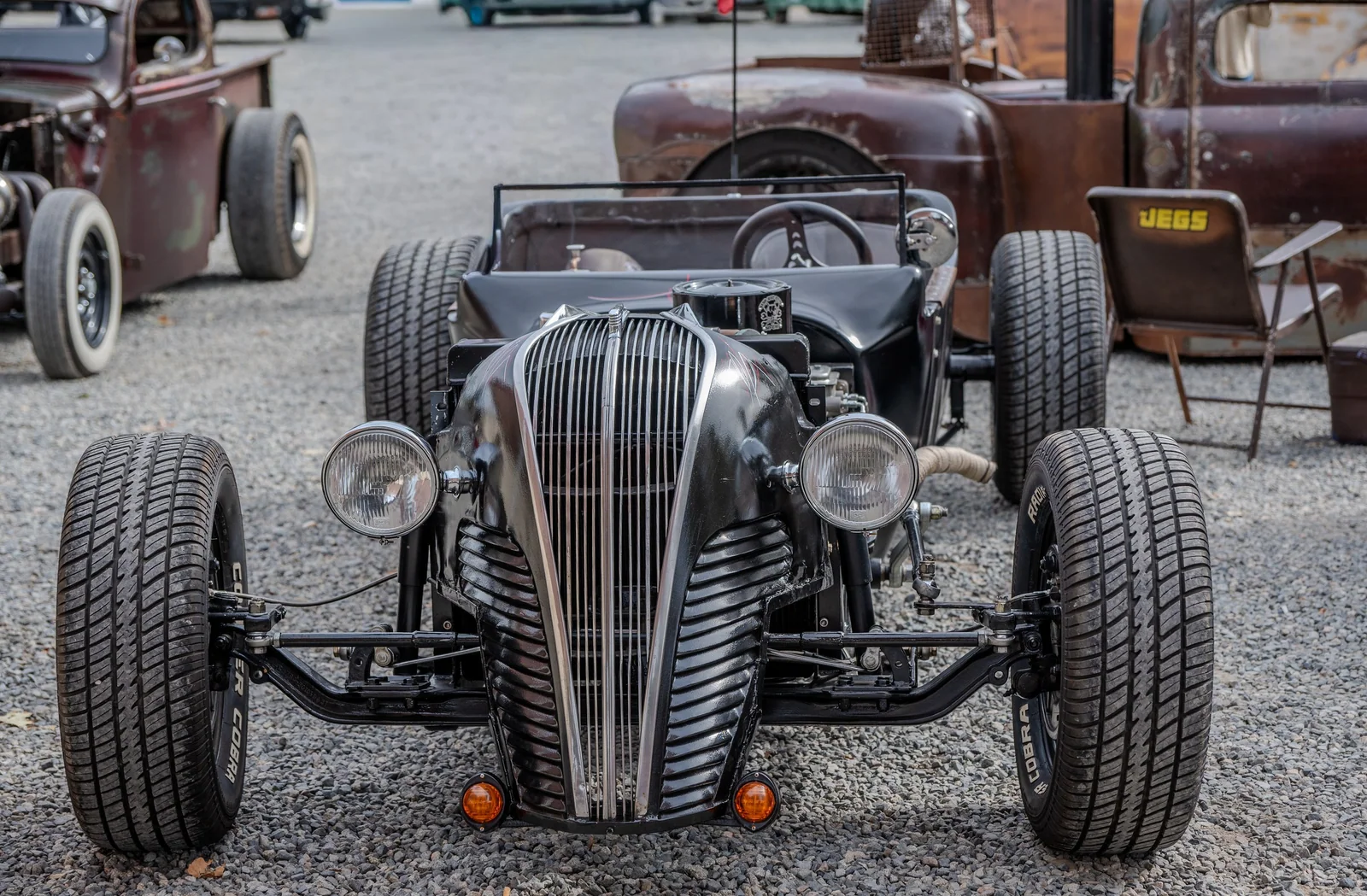 Black open-top rat rod seen head-on, with an exposed axle and widely spaced tires.