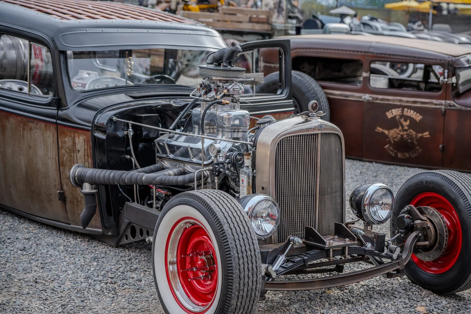 Rat rod with polished exposed engine, wrapped exhausts, red wheels, and whitewall tires.