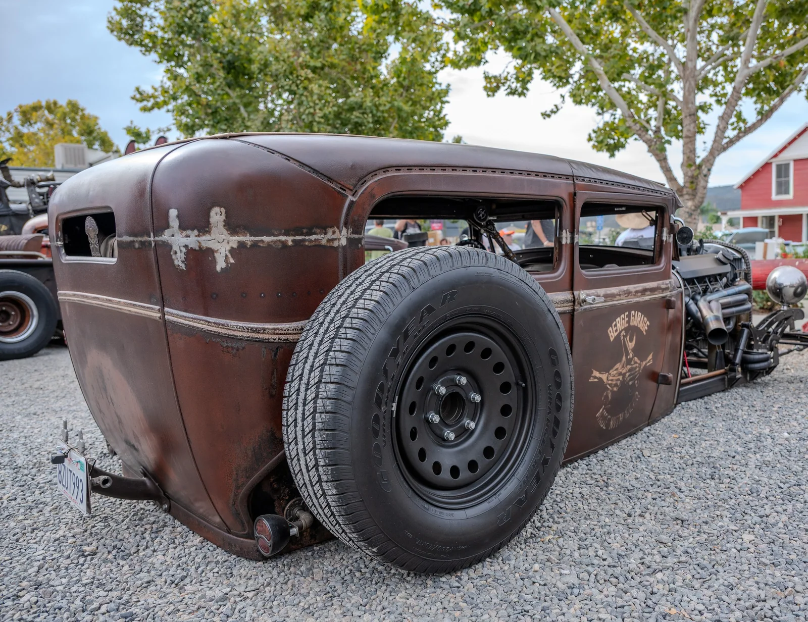 Patinated brown rat rod body beside a large black rear tire.