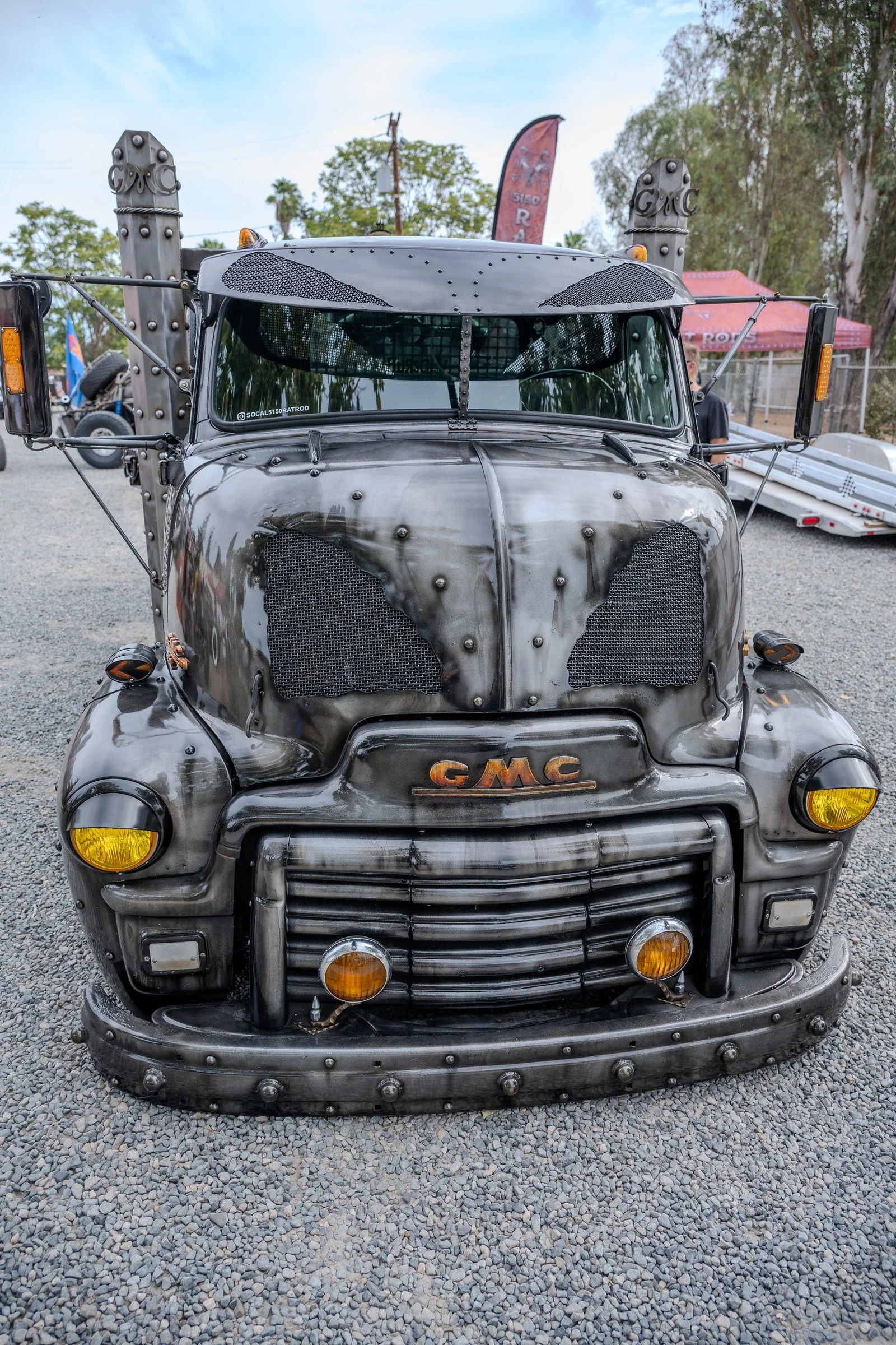 Modified weathered GMC truck seen head-on, with mesh, rivets, and yellow lamps.