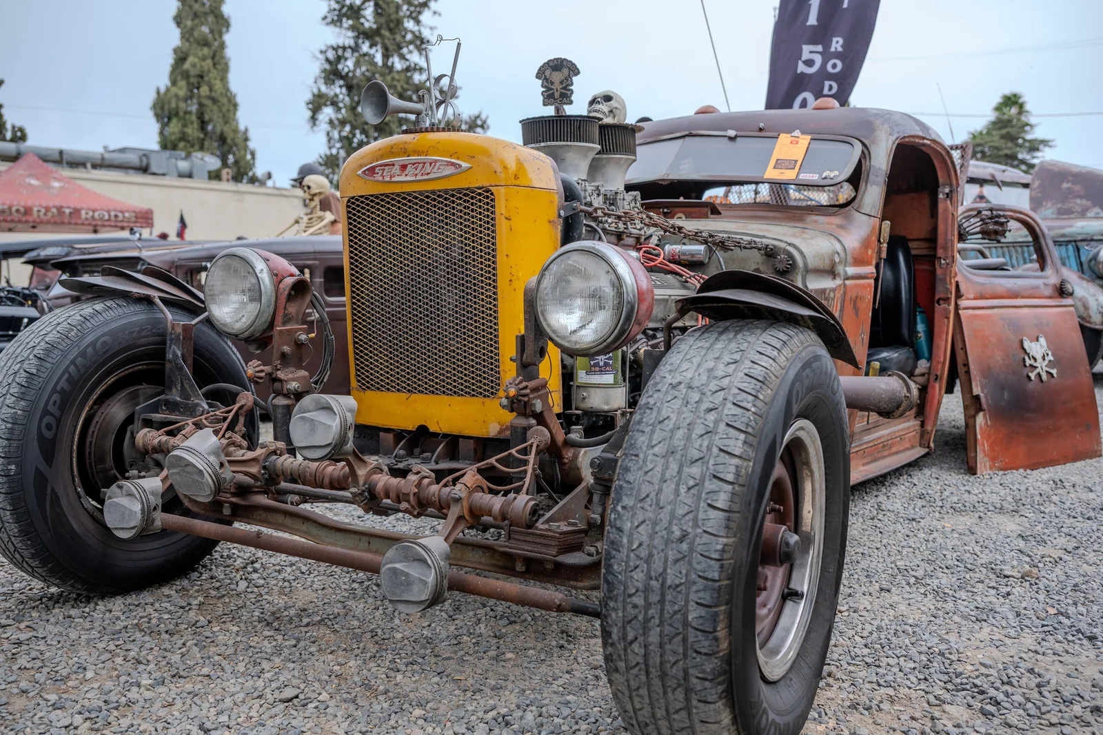 Weathered rat rod with a yellow grille, exposed front suspension, and wide front tires.