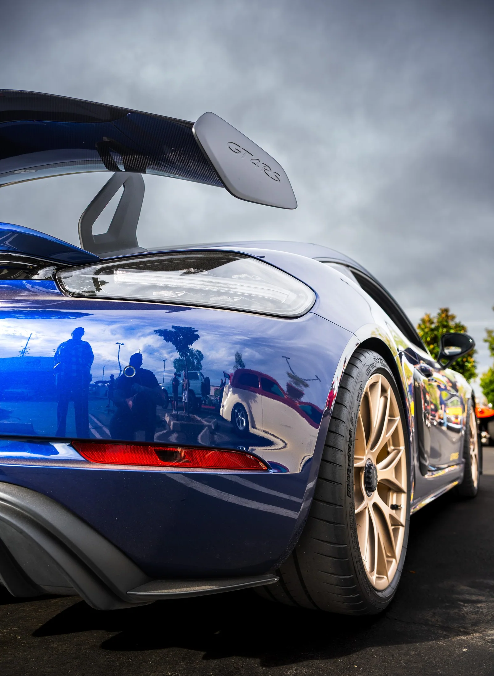 Blue Porsche Cayman rear quarter, wing, and bronze rear wheel.
