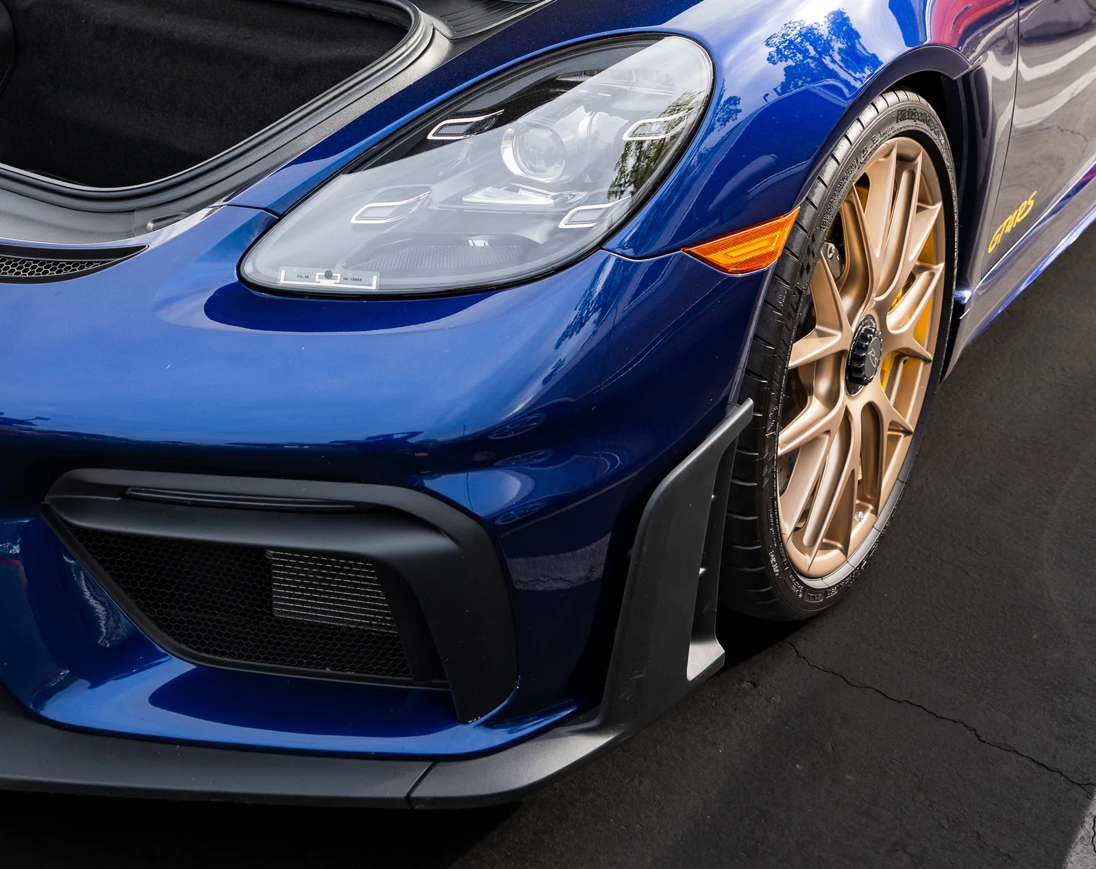 Blue Porsche Cayman GT4 RS front quarter with a headlamp, aerodynamic intake, and bronze wheel.