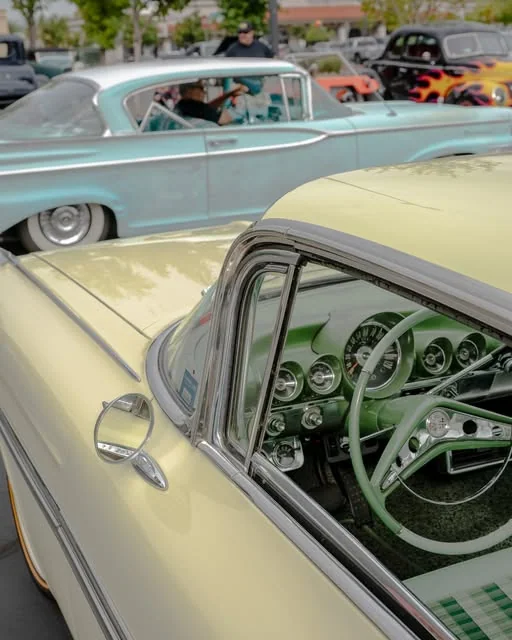Light-green steering wheel and instruments through an open window, with cars behind.